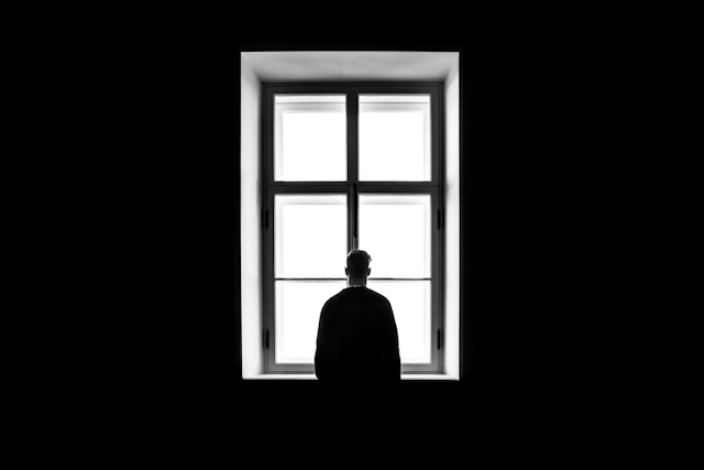 man standing in front of a window in a dark-black room.