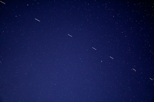Picture of the night skies with stars in the background and lines of satellites moving across the sky from bottom right to top left.