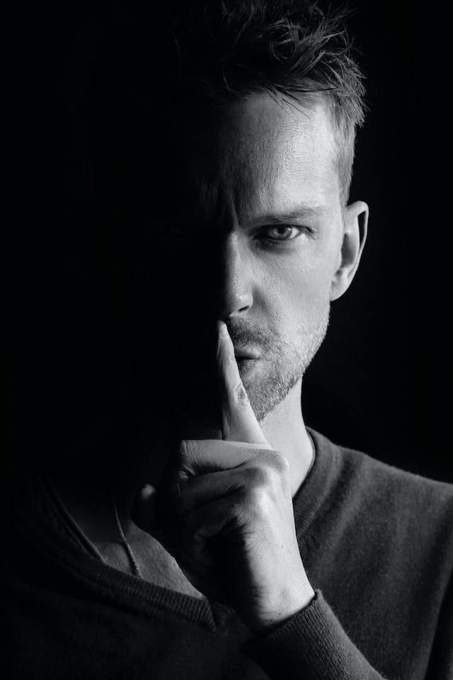 Black and white picture of a man with his finger to his mouth, shush up and keep quite.